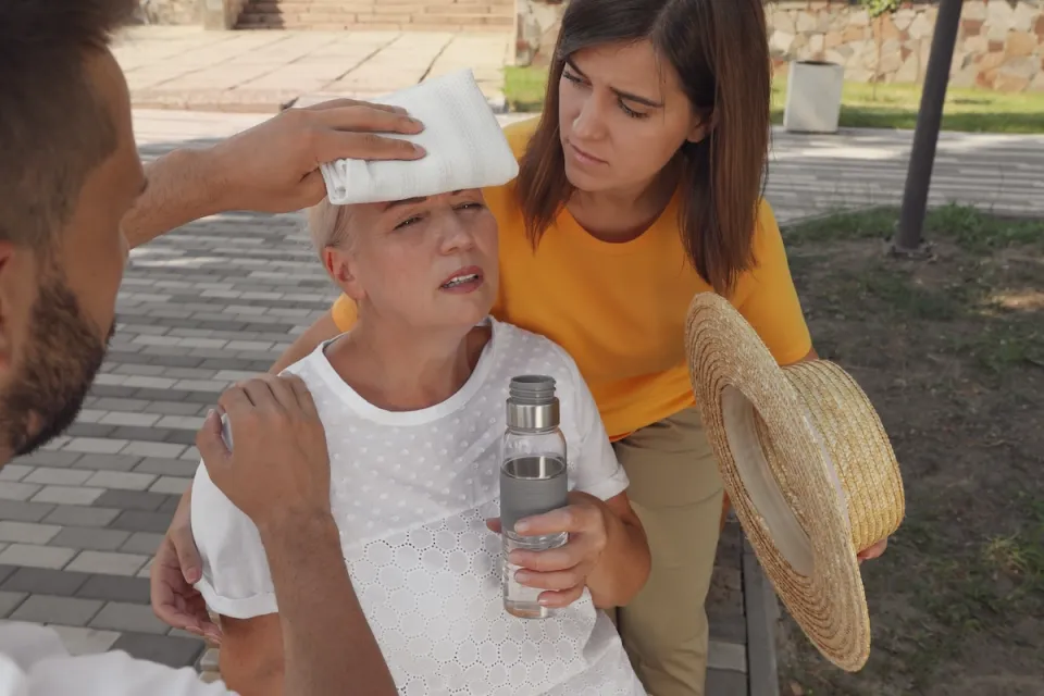 Two people helping an older woman outdoors suffering from heat stroke.